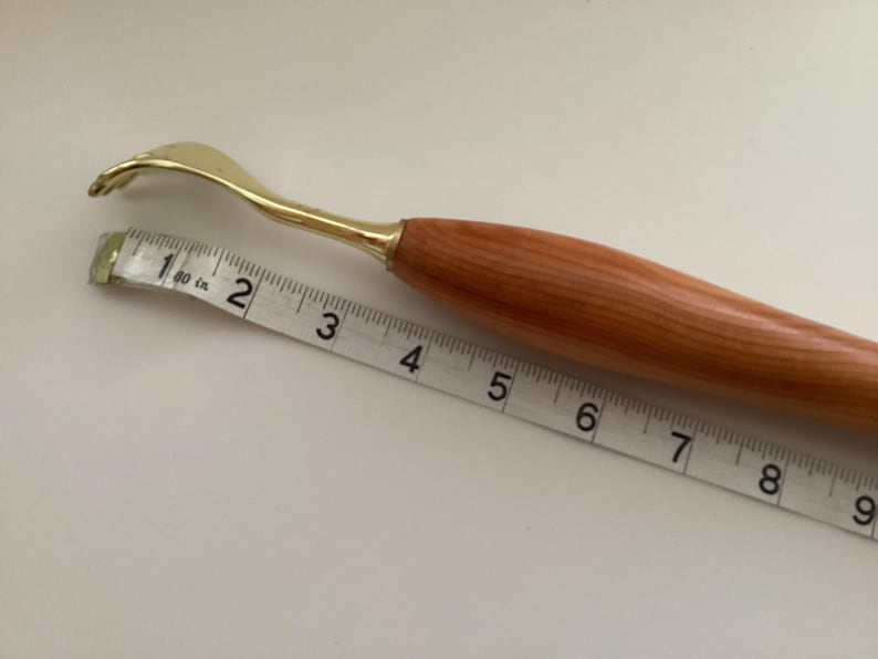 May include: A wooden handled back scratcher with a gold metal hook. The scratcher is 15 cm long and is measured against a tape measure.