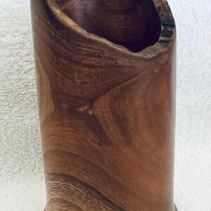 May include: A cylindrical wooden vessel with a natural live edge rim and visible wood grain patterns. A yellow ruler is positioned inside the opening, indicating a height measurement of approximately 6.5 inches from the base to the highest point.