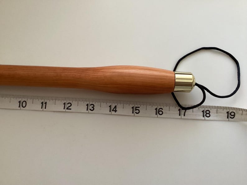 May include: A wooden knitting needle with a gold-coloured tip and a black cord loop. The needle is 17 inches (43 cm) long.