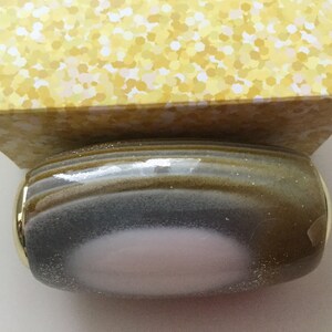 May include: A round, gray and gold bottle stopper with a pink center. The bottle stopper has a textured, speckled surface.