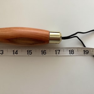 May include: A wooden knitting needle with a brass tip and a black cord attached. The needle is 40.6 cm long.