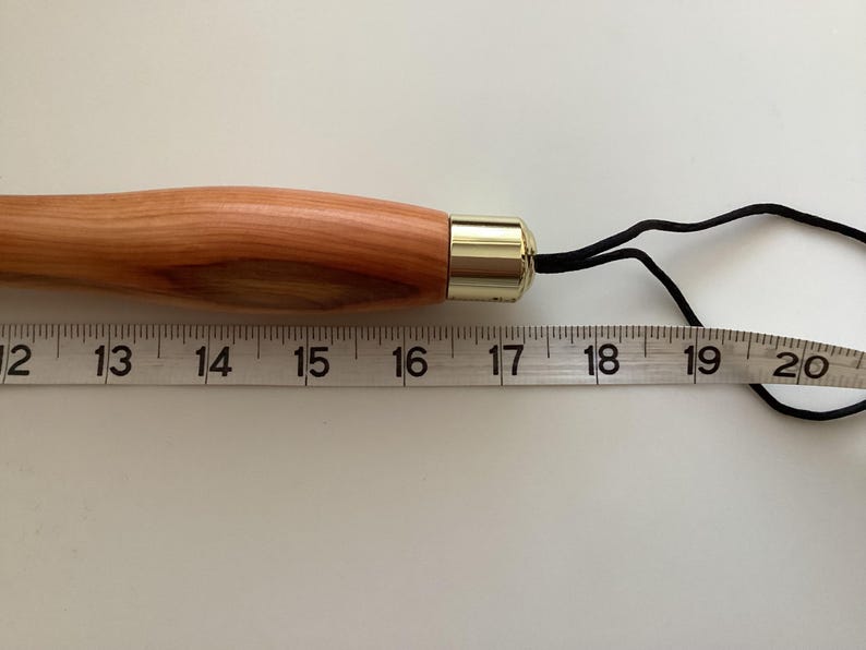 May include: A wooden knitting needle with a brass tip and a black cord attached. The needle is 40.6 cm long.