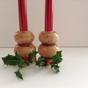 May include: Two wooden candle holders with red candles. The holders are made of natural wood and have a rustic look. The candles are surrounded by green holly leaves and red berries.