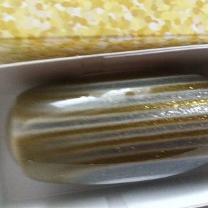 May include: A gold and silver striped decorative object with glitter. The object is in a white box with a yellow patterned lid.