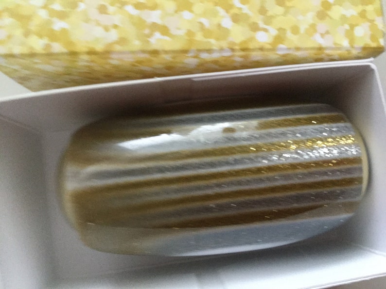May include: A gold and silver striped decorative object with glitter. The object is in a white box with a yellow patterned lid.