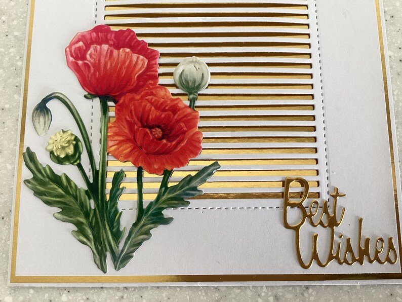 May include: A greeting card featuring red poppy flowers and green leaves. The background has gold horizontal stripes and the words "Best Wishes" in gold script. The card has a gold border.