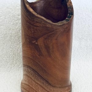 May include: A cylindrical wooden vessel with a natural, uneven live edge rim and a smooth, polished brown grain. A yellow ruler is positioned behind the object, showing a height measurement that reaches the 10-inch mark on the scale.