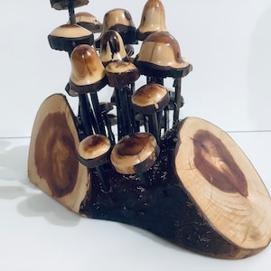 May include: A wooden sculpture of a cluster of mushrooms growing from a tree stump. The mushrooms are made of wood and have a natural brown and beige colour. The tree stump is also made of wood and has a natural brown colour.