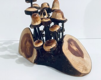 May include: A wooden sculpture of a cluster of mushrooms growing from a tree stump. The mushrooms are made of wood and have a natural brown and beige color. The tree stump is also made of wood and has a natural brown color.