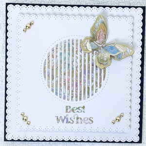 May include: A handmade greeting card with a butterfly design. The card features a white scalloped edge, a cut-out circle with vertical stripes, and the words "Best Wishes". Gold embellishments are placed on the corners.