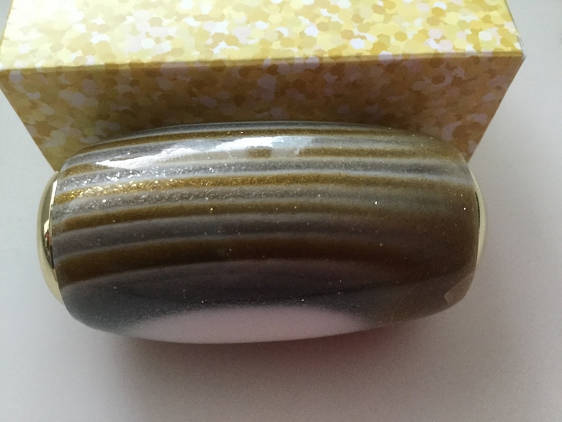 May include: A gold and silver striped cylindrical bottle stopper with a gold rim.
