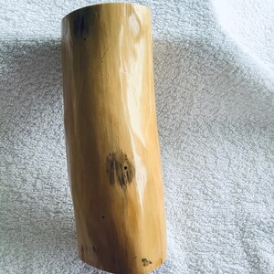 May include: A light brown wooden vase with a natural, organic shape and a smooth, polished finish. The vase has a few dark brown knots and markings on its surface.