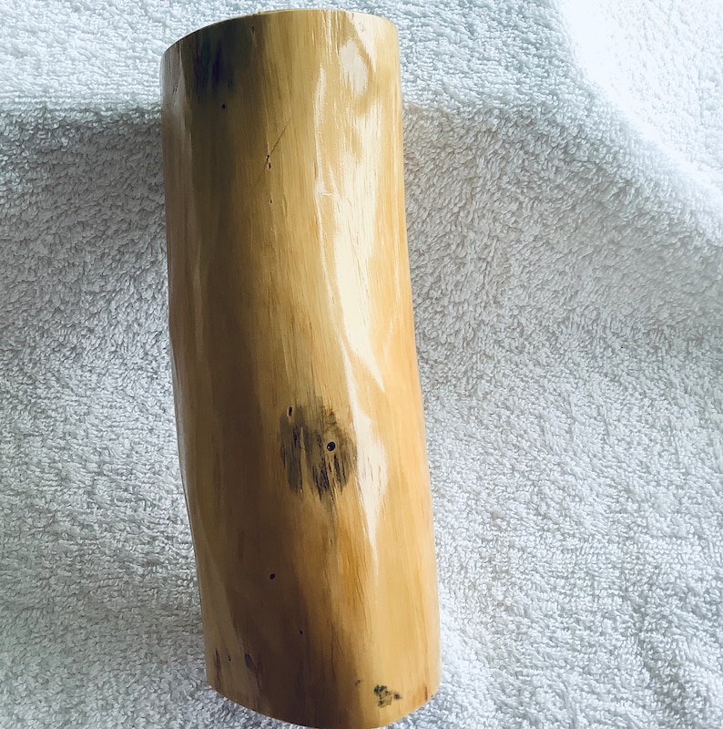 May include: A light brown wooden vase with a natural, organic shape and a smooth, polished finish. The vase has a few dark brown knots and markings on its surface.