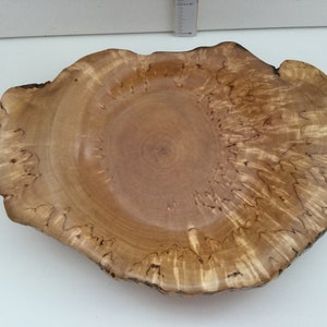 May include: A large, wooden bowl with a natural, light brown finish. The bowl has a unique, irregular shape and a smooth, polished surface. The wood grain is visible and adds to the rustic charm of the bowl.