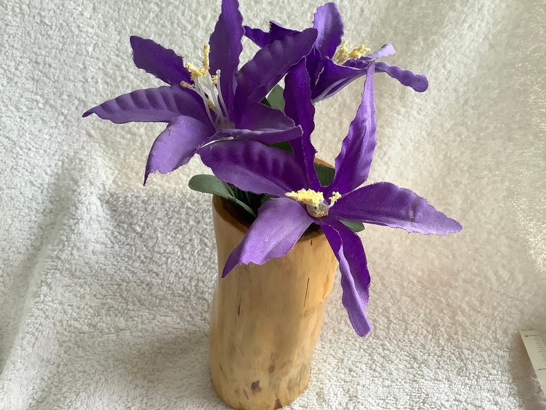 May include: Purple artificial flowers in a wooden vase. The vase is made from a natural log and has a rustic look.