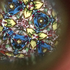 May include: A kaleidoscope image with a symmetrical pattern of blue, yellow, green, and red shapes. The image is created by reflecting light through a series of mirrors.
