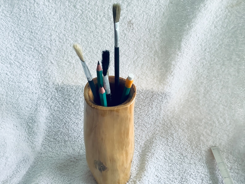 May include: A wooden pencil holder with a natural finish. It holds a variety of art supplies, including paintbrushes and pencils.