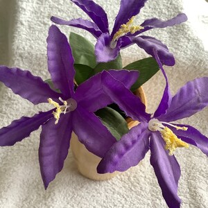 May include: A bouquet of purple silk flowers with yellow centres in a brown ceramic pot.