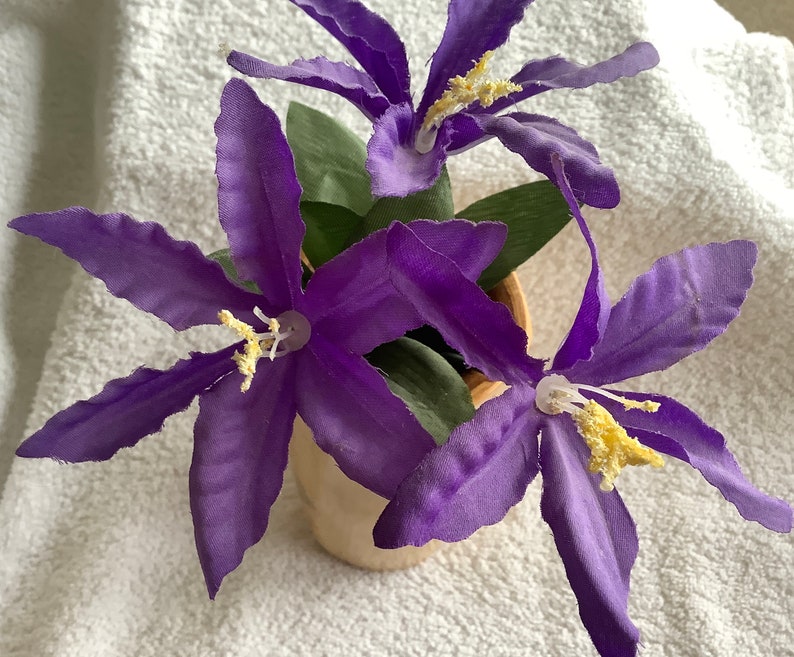 May include: A bouquet of purple silk flowers with yellow centres in a brown ceramic pot.