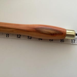 May include: A wooden dowel rod with a brass tip and a black cord attached. The rod is approximately 40 cm long.