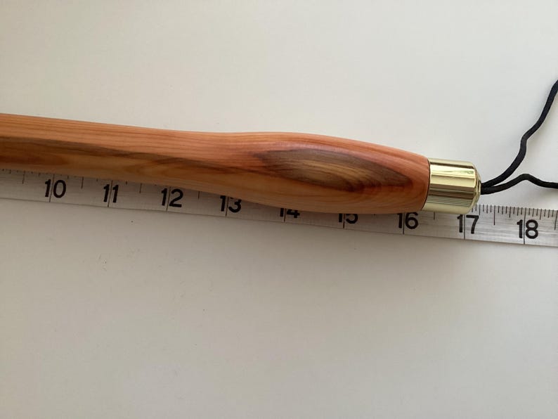 May include: A wooden dowel rod with a brass tip and a black cord attached. The rod is approximately 40 cm long.