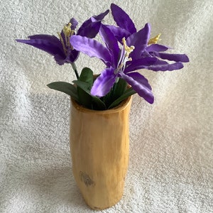 May include: A wooden vase with a natural, rustic finish holds a bouquet of purple silk flowers.