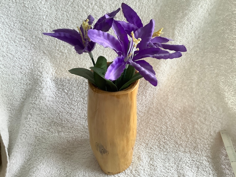May include: A wooden vase with a natural, rustic finish holds a bouquet of purple silk flowers.