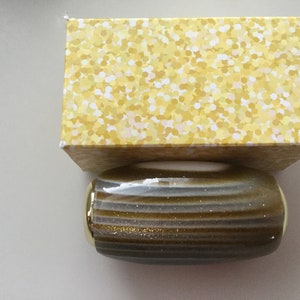 May include: A gold and gray striped cylindrical container with gold accents. The container is sitting on top of a yellow box with a white polka dot pattern.