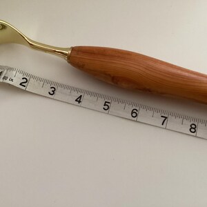 May include: A wooden and gold back scratcher with a long handle and a claw-like end. The scratcher is measured against a tape measure, showing it is approximately 18 cm long.