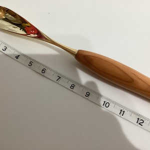 May include: A gold-colored metal spoon with a wooden handle. The spoon is about 12 inches long.
