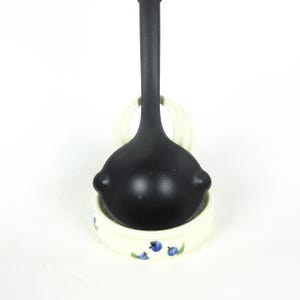 Puede incluir: Un cuchar&oacute;n negro con un soporte para cuchar&oacute;n de cer&aacute;mica blanca con un dise&ntilde;o de ar&aacute;ndanos azules.