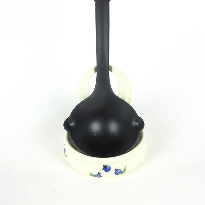 Puede incluir: Un cuchar&oacute;n negro con un soporte para cuchar&oacute;n de cer&aacute;mica blanca con un dise&ntilde;o de ar&aacute;ndanos azules.