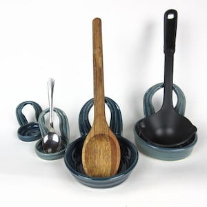 May include: A blue ceramic spoon rest with three separate holders for spoons, a wooden spoon, and a black ladle.