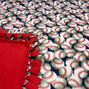 May include: A red fleece tie blanket with a baseball pattern border. The blanket is made with a knotted fringe.