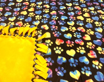 May include: A yellow fleece tie blanket with a black fleece backing. The backing has a colorful tie-dye pattern of hearts and paw prints.