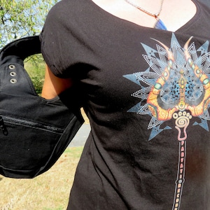 May include: Black shoulder bag with a zippered pocket and a curved strap. The bag is made of a sturdy material and has metal grommets. A black t-shirt with a colorful graphic print is also visible.