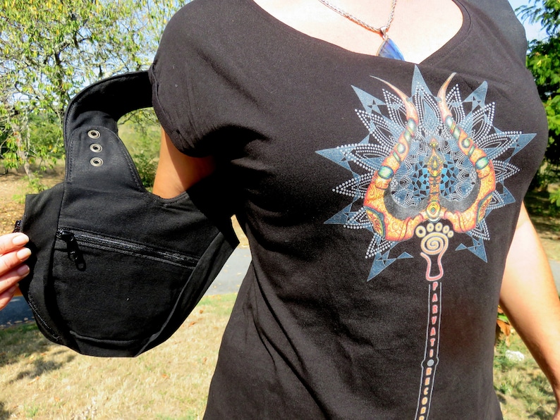 May include: Black shoulder bag with a zippered pocket and a curved strap. The bag is made of a sturdy material and has metal grommets. A black t-shirt with a colorful graphic print is also visible.