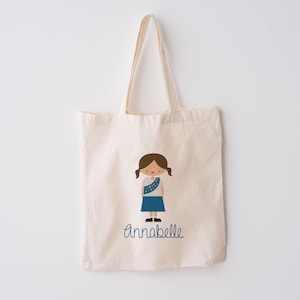 May include: A white canvas tote bag with a blue and brown illustration of a girl scout. The bag has the name "Annabelle" printed in blue cursive.