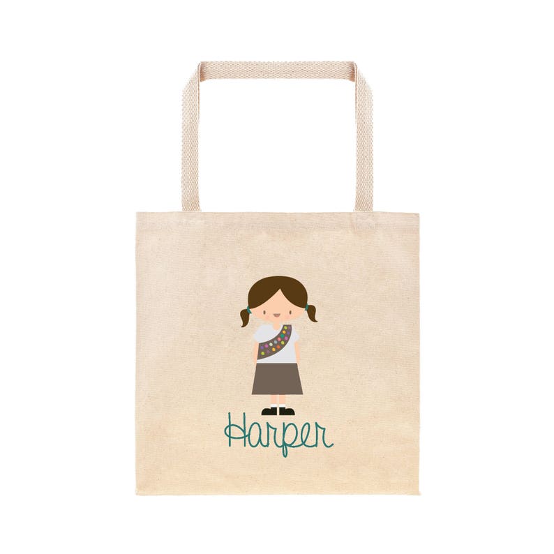 May include: A beige tote bag featuring a brown girl guide character and the name "Harper" in teal text.