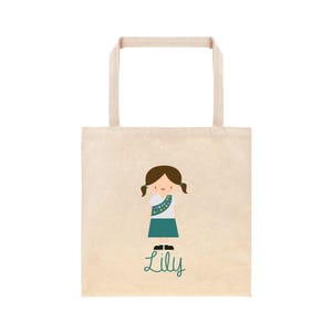 May include: A beige tote bag featuring a cartoon illustration of a girl scout wearing a green sash and a white shirt. The girl has brown hair and is smiling. The text "Lily" is written in green below the illustration.
