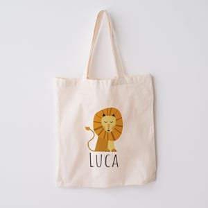 May include: A beige canvas tote bag with a lion illustration and the name "LUCA" printed in black.