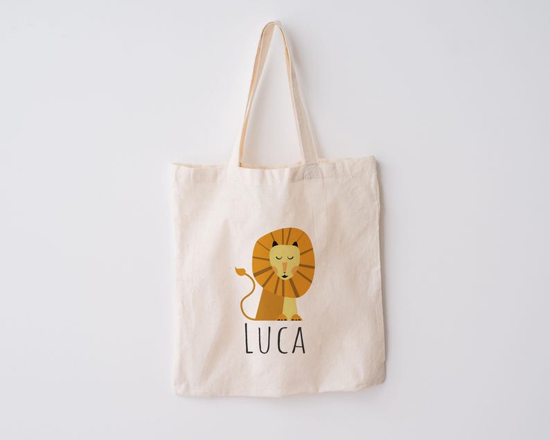 May include: A beige canvas tote bag with a lion illustration and the name "LUCA" printed in black.