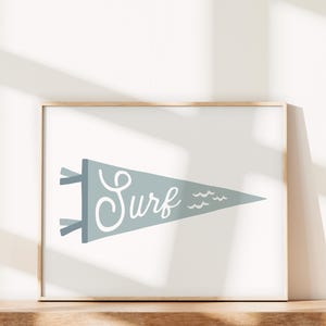 May include: A framed print of a blue pennant with the word "Surf" in white script and white wavy lines. The print is on a white background.