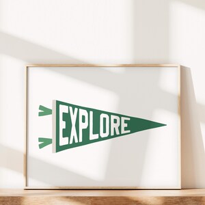 Könnte beinhalten: Ein gerahmter Druck eines grünen Wimpels mit dem Wort "EXPLORE" in weißen Buchstaben. Der Wimpel hängt an einer weißen Wand.