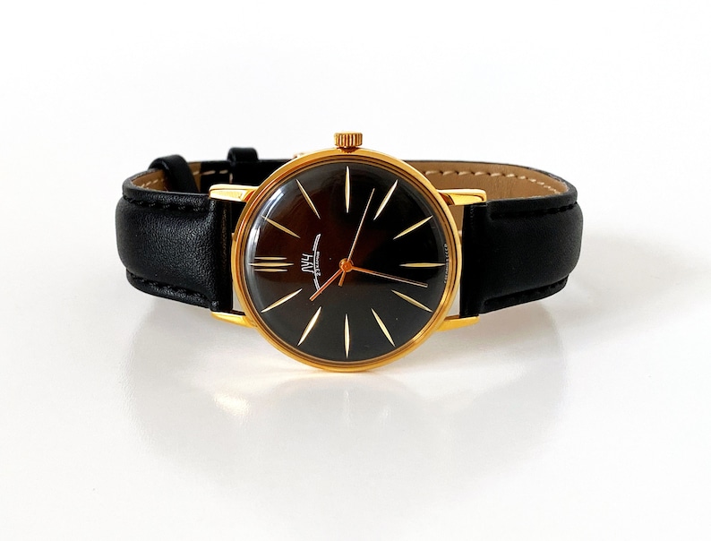 May include: A gold-tone wristwatch with a black leather band and a black face with gold-tone hands and hour markers. The watch face has the word "Poljot" printed on it.