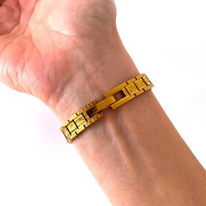 K&ouml;nnte beinhalten: Ein goldfarbenes Armband mit strukturierter Oberfl&auml;che. Das Armband ist aus Metall und hat einen Verschluss.