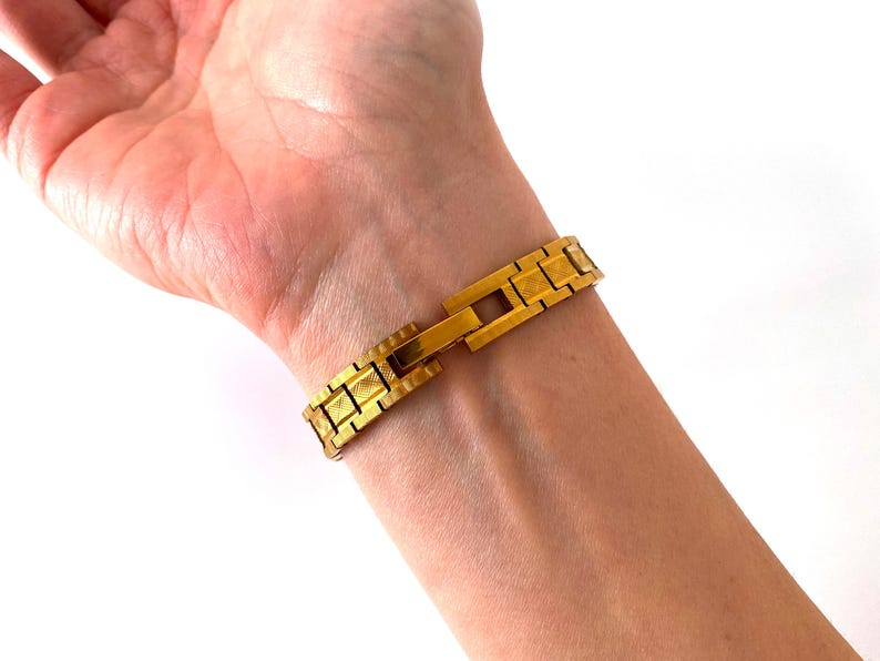 K&ouml;nnte beinhalten: Ein goldfarbenes Armband mit strukturierter Oberfl&auml;che. Das Armband ist aus Metall und hat einen Verschluss.