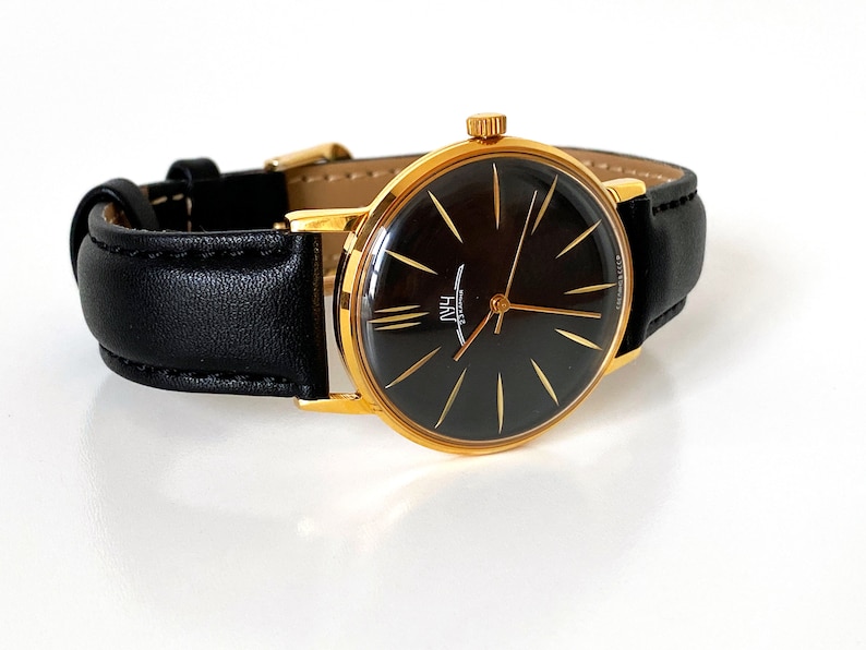 May include: A gold-tone wristwatch with a black face and gold hands. The watch has a black leather band.