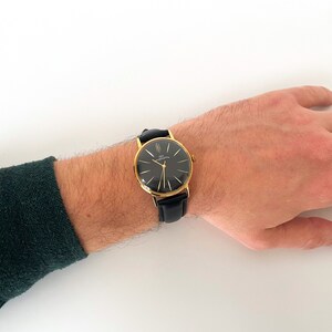 May include: A gold-tone wristwatch with a black face and black leather band.