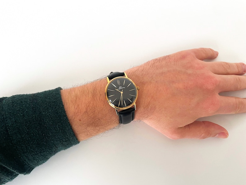 May include: A gold-tone wristwatch with a black face and black leather band.
